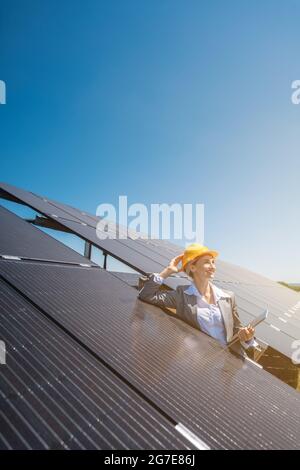 Femme d'affaires ou investisseur inspectant sa ferme solaire debout devant des panneaux photovoltaïques Banque D'Images
