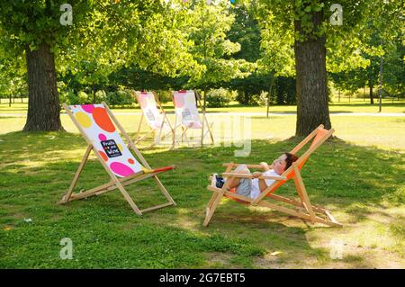 POZNAN, POLOGNE - 19 juillet 2017 : un enfant repose sur une chaise de parc en bois à l'ombre d'un arbre à Jan Pawla Banque D'Images