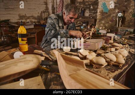 Homme mature menuisier faisant des jouets en bois en atelier, Craftsman en action, ancien artiste au travail Banque D'Images