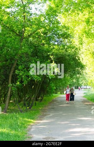 POZNAN, POLOGNE - 22 mai 2014 : un sentier le long de l'herbe verte et des arbres et deux femmes marchant dans un parc de la région de Piastowskie Banque D'Images