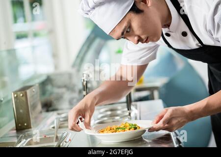 Un chef cuisinier prépare un plat de nourriture dans un restaurant asiatique en essuyant soigneusement les côtés de la plaque pour éviter tout déversement Banque D'Images