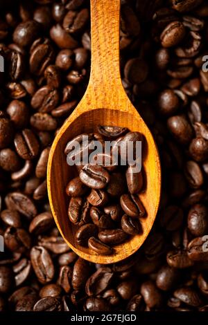 Une cuillère en bois contenant quelques grains de café. La cuillère est en cours de dégustation sur beaucoup de grains de café Banque D'Images
