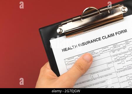 Contrat d'assurance maladie en main et presse-papiers. Arrière-plan rouge bordeaux. Document de santé et d'affaires Banque D'Images