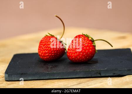 Fraises mûres rouges sur une petite planche à découper noire sur une table en bois Banque D'Images