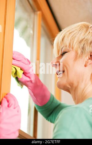 Femme mûre nettoyant ses fenêtres dans un Spring-Clean, elle porte des gants en caoutchouc et semble plutôt gai malgré la tâche Banque D'Images