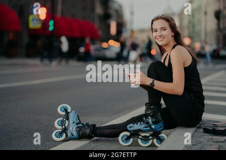 Personnes activités de plein air et concept de loisirs. Plan horizontal de femme active mince étant en bonne forme physique manèges rollerblades utilise un smartphone Banque D'Images