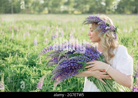 Une fille hippie tenant un bouquet de fleurs sauvages dans ses mains. Une fille cacha son visage derrière un bouquet de lupins. La fille tient un grand bouquet de lupins violets dans un Banque D'Images