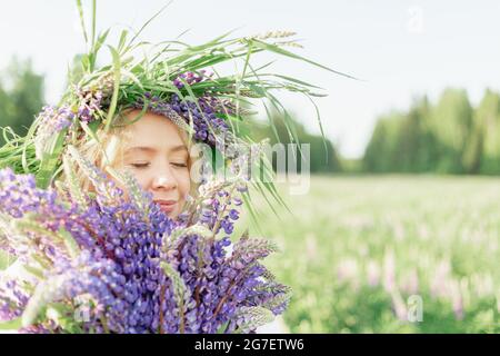 Une fille hippie tenant un bouquet de fleurs sauvages dans ses mains. Une fille cacha son visage derrière un bouquet de lupins. La fille tient un grand bouquet de lupins violets dans un Banque D'Images