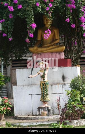 Une statue de Phra Mae Thorani lavant ses cheveux devant une statue de Bouddha assise, Luang Prabang, Laos Banque D'Images