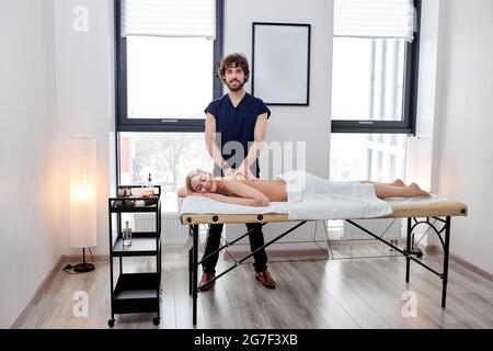 Portrait de Nice Masseur barbu en uniforme faisant avec soin massage sur le dos femelle, femme blanche Blonde couché sur le ventre relaxant, appréciant. Station santé Copy Banque D'Images