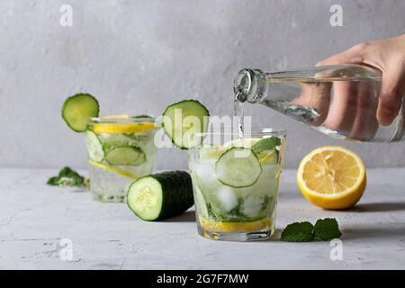 Deux boissons fraîches fraîches d'été avec menthe, citron et concombre, cocktail de mojito de Detox sain sur fond gris clair. L'eau minérale est versée à partir d'un bott Banque D'Images