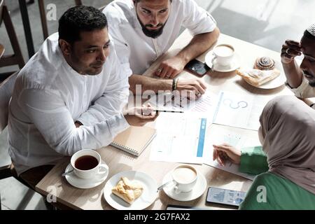 Groupe de collègues musulmans assis à la table et discutant du rapport dans un café Banque D'Images