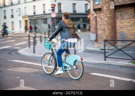 Un homme n un vélo loué avec un moteur électrique pour les voyages en ville se déplace dans une rue dans le vieux Paris préférant un style de vie sain en utilisant le vélo et cycl Banque D'Images
