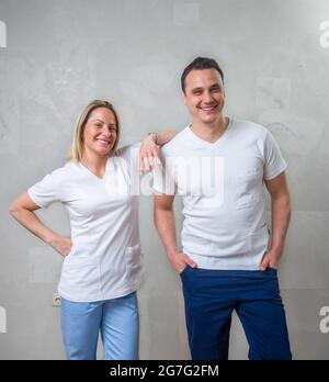 deux personnes, une équipe de physiothérapeutes, des collègues souriants portrait. debout devant un mur gris. Banque D'Images