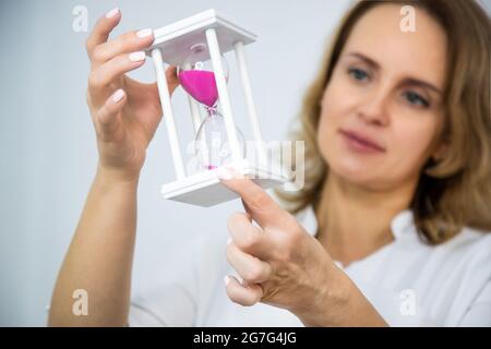 Le médecin tient un sablier en verre dans les bras étirés au premier plan. Banque D'Images