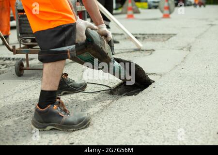 Il enlève l'asphalte avec un marteau à inertie. Retrait de la couche d'asphalte de la route. Le travailleur tient un marteau à inertie. Réparation sur route. Utilisation d'un hammam électrique Banque D'Images