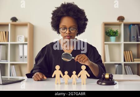 La juge féminine afro-américaine regarde à travers une loupe les figurines en bois d'une famille. Banque D'Images