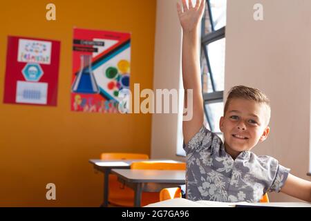 Un bon élève du caucase assis à un bureau en classe, levant la main pendant la leçon Banque D'Images