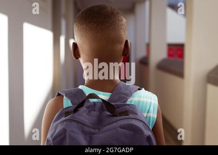 Vue arrière d'un écolier afro-américain portant un sac d'école debout dans le couloir de l'école Banque D'Images
