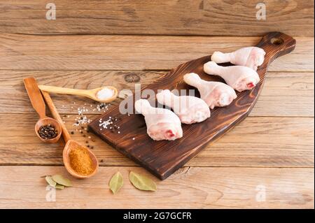 Pilons de poulet crus avec persil et épices sur une planche à découper en bois. Vue de dessus. Banque D'Images