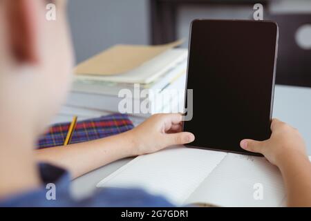 Un élève de race blanche en classe assis au bureau à l'aide d'une tablette, avec un espace de copie à l'écran Banque D'Images