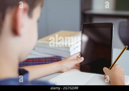 Un élève de race blanche en classe assis au bureau à l'aide d'une tablette, avec un espace de copie à l'écran Banque D'Images