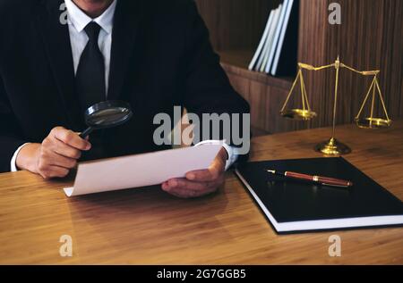 Un avocat de sexe masculin lit l'accord de contrat légal et examine des documents avec une loupe dans la salle d'audience. Banque D'Images