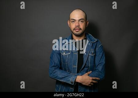 Portrait d'un jeune homme chauve mexicain élégant portant une veste en denim posant sur un fond gris Banque D'Images