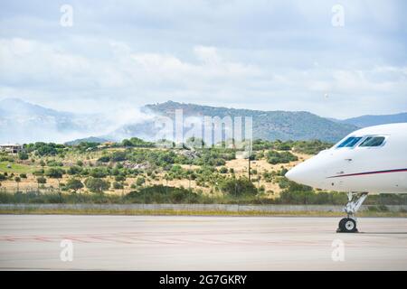 Vue sur un incendie dans les environs de l'aéroport d'Olbia Costa Smeralda avec des avions stationnés sur la piste Banque D'Images