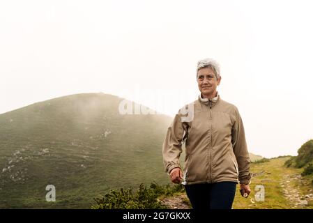 Voyageur âgé avec de courts cheveux gris qui regarde loin et marche sur le sentier près de la colline en journée dans la nature Banque D'Images