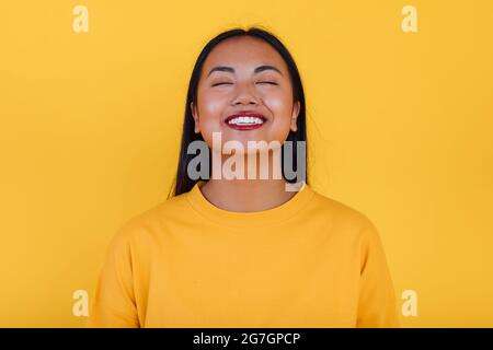 Femme asiatique ravie debout sur fond jaune en studio avec les yeux fermés Banque D'Images