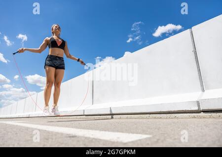 Jeune femme s'entraîner avec la corde à sauter extérieure, vue latérale Banque D'Images