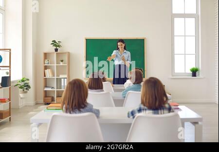 Une enseignante souriante et heureuse pose une question à son petit élève du primaire en classe Banque D'Images