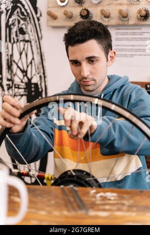 Un mécanicien sérieux fixe les rayons de roue lorsqu'il est assis à l'établi en service de vélo Banque D'Images