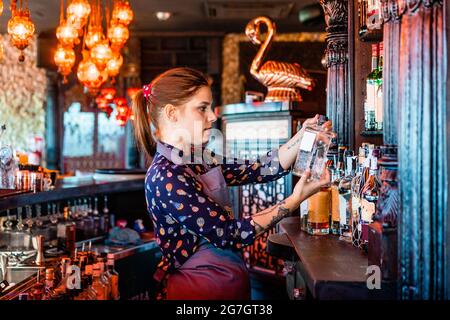 Vue latérale d'une femme barman qui choisit l'alcool dans une bouteille pour préparer un cocktail au bar Banque D'Images