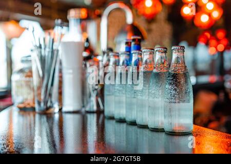 Bouteilles en verre avec eau froide rafraîchissante placées en rangée sur un comptoir en bois dans le bar Banque D'Images