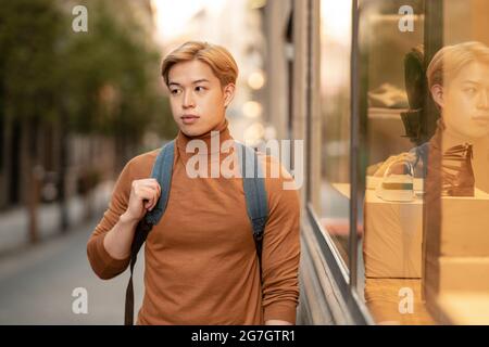 Modèle ethnique homme confiant avec cheveux blonds et dans le turtleneck tendance debout en ville et regardant la caméra Banque D'Images