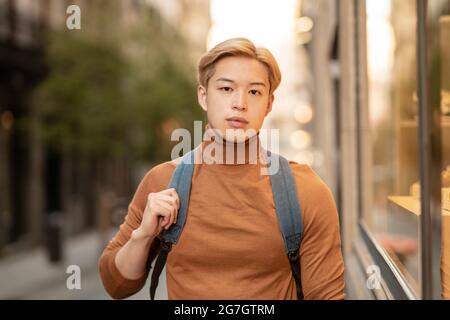 Modèle ethnique homme confiant avec cheveux blonds et dans le turtleneck tendance debout en ville et regardant la caméra Banque D'Images