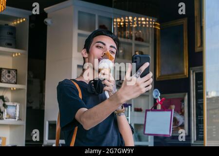 Contenu gay homme manger de la glace douce et prendre le coup de soi sur le téléphone mobile dans la ville Banque D'Images