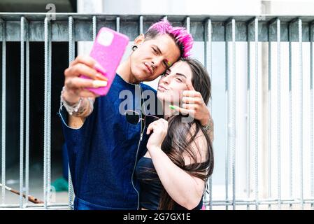 Homme gay tendance et femme élégante prenant autoportrait sur téléphone mobile tout en se tenant dans la rue Banque D'Images