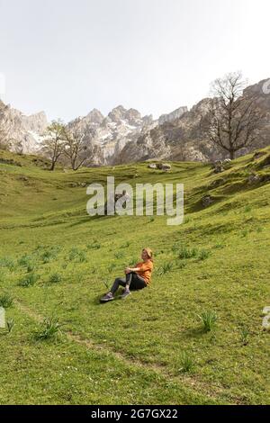 Vue latérale d'une randonneur femelle calme, assise sur une colline verdoyante et herbeuse, et profitant de la paix et de la solitude, tout en se reposant après une randonnée à travers les Picos de Europa mou Banque D'Images