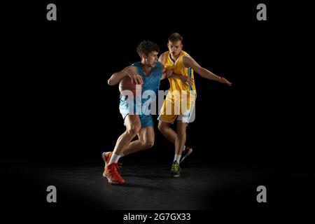 Deux joueurs de basket-ball en action et en mouvement isolés sur fond noir foncé de studio. Concept publicitaire. Des athlètes caucasiens forts pratiquant avec Banque D'Images