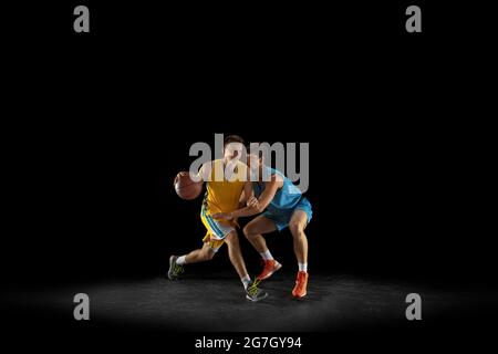 Deux joueurs de basket-ball en action et en mouvement isolés sur fond noir foncé de studio. Concept publicitaire. Des athlètes caucasiens forts pratiquant avec Banque D'Images