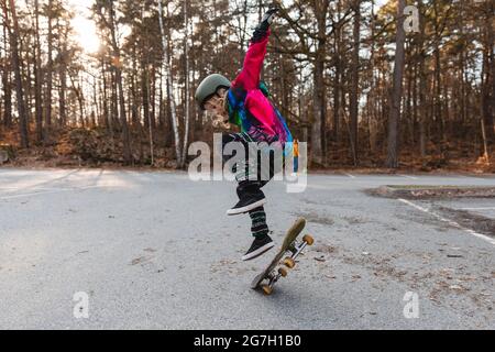 Vue latérale d'une jeune patineuse talentueuse sautant avec un skateboard dans le parc en automne Banque D'Images
