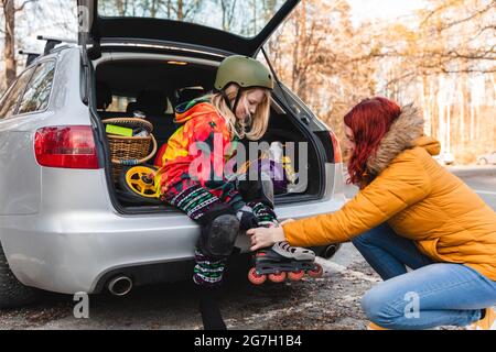Vue latérale de la mère aidant la fille à mettre sur les rollerblades tout en étant assis dans le coffre de voiture Banque D'Images