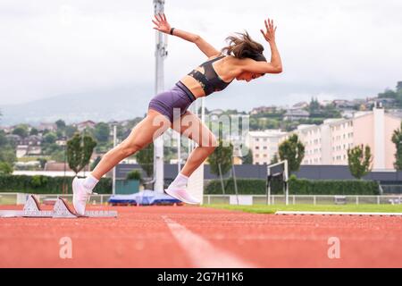 Vue latérale complète du jeune sprinter féminin déterminé commençant à courir à partir de blocs sur la piste du stade Banque D'Images