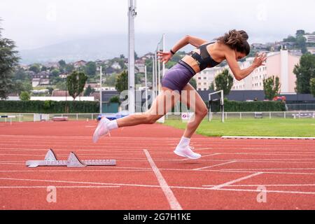 Vue latérale complète du jeune sprinter féminin déterminé commençant à courir à partir de blocs sur la piste du stade Banque D'Images