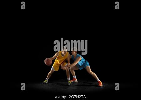 Deux joueurs de basket-ball en action et en mouvement isolés sur fond noir foncé de studio. Concept publicitaire. Des athlètes caucasiens forts pratiquant avec Banque D'Images