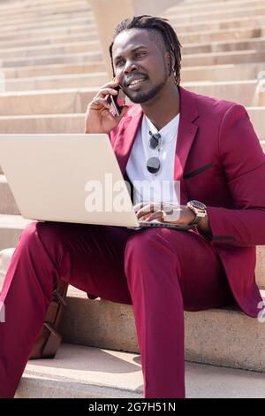 l'homme d'affaires africain travaille avec un ordinateur portable et un téléphone assis sur les escaliers de la ville, la technologie et le concept de travail à distance Banque D'Images