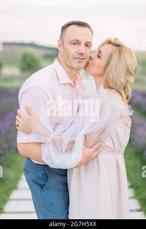 Couple amoureux mûr et romantique marchant dans le champ de lavande. Couple d'âge moyen de race blanche rêveuse et heureuse dans la nature, debout tenant les mains. Femme embrassant son homme. Profitez de l'instant présent. Banque D'Images